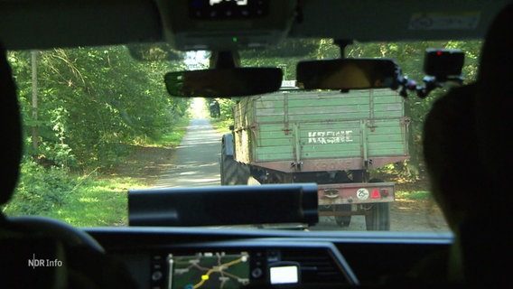 Durch die Frontscheibe eines Autos ist ein Traktor mit Anhänger zu sehen. © Screenshot 