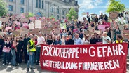 Auf einer Demo wird ein Banner mit der Aufschrift: "Psychotherapie in Gefahr - Weiterbildung finanzieren" getragen. © Screenshot 