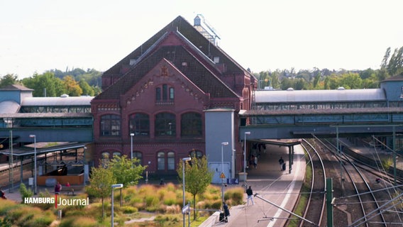 Das historische Bahnhofsgebäude in Harburg mit rotem Mauerwerk, umgeben von Gleisen und Pflanzen. © Screenshot 