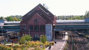 Das historische Bahnhofsgebäude in Harburg mit rotem Mauerwerk, umgeben von Gleisen und Pflanzen. © Screenshot 