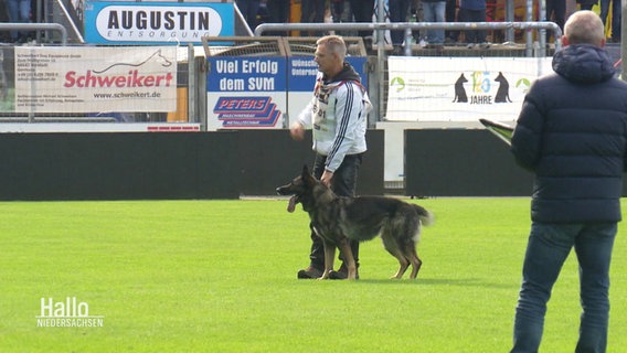 Ein Mann und sein Schäferhund stehen auf einer Rasenfläche. © Screenshot 