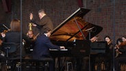 Der Pianist Rafał Blechacz spielt auf einer Bühne mit der NDR Elbphilharmonie. © Screenshot 