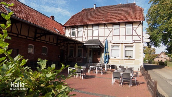 Eine Gaststätte in einem Fachwerkhaus im Sonnenschein. Vor dem Haus eine Terrasse mit Tischen und Stühlen. © Screenshot 