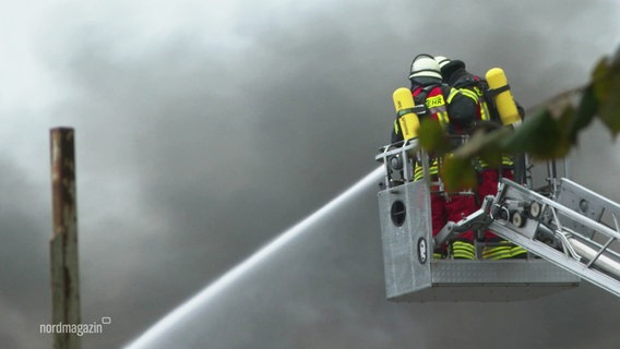 Feuerwehrleute stehen auf der ausgefahrenen Leiter eines Einsatzwagens und löschen einen Brand. © Screenshot 