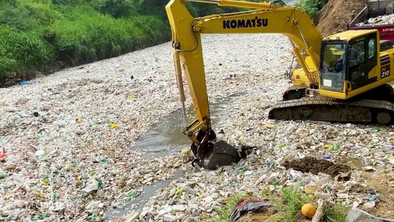 Ein Bagger schaufelt eine endlose Flut an Müll aus einem Fluss. © Screenshot 