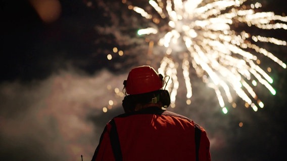 Ein Mensch mit Schutzhalm in Rückansicht blickt auf Feuerwerk am Himmel © Screenshot 