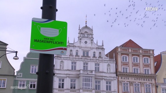 Eine Häuserzeile, davor ein Schild mit der Aufschrift "Hier gilt Maskenpflicht!". © Screenshot 