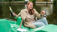 Reporterin Céline in einem Tretboot auf der Alster mit einer Champagnerflasche und Glas. (extra 3 vom 10.10.2024 im Ersten) © NDR 