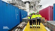 Menschen in Neongelb/dunklen Anzügen mit Grünen Helmen auf einem Schiff. © Screenshot 