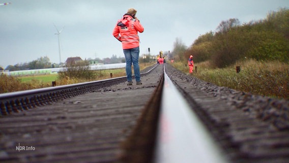 Eine Person in Warnfarbe steht auf einem Gleis. © Screenshot 