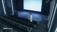 Ein leeres kleines Kino mit erleuchteter Leinwand, zwei Personene setzen sich in die zweite Reihe. © Screenshot 