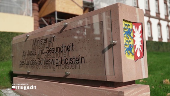 Stein mit Schild: "Ministerium für Justiz und Gesundheit des Landes Schleswig-Holstein" sowie dem schleswig-holsteinischen Wappen. © Screenshot 