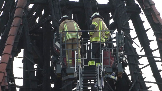 Zwei Feuerwehrmänner in einem Steigerkorb der Feuerwehr vor dem verkohlten und abgrebrannten Kirchturm der Dionysiuskirche in Bremerhaven. © Screenshot 