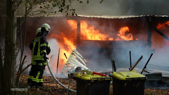 Ein Feuer wütet an einem Haus und zwei Rettungskräfte versuchen den Brand zu löschen. © Screenshot 