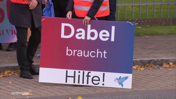 Eine demonstrierende Person hält ein Schild mit der Aufschrift "Dabel braucht Hilfe". © Screenshot 