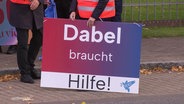 Eine demonstrierende Person hält ein Schild mit der Aufschrift "Dabel braucht Hilfe". © Screenshot 