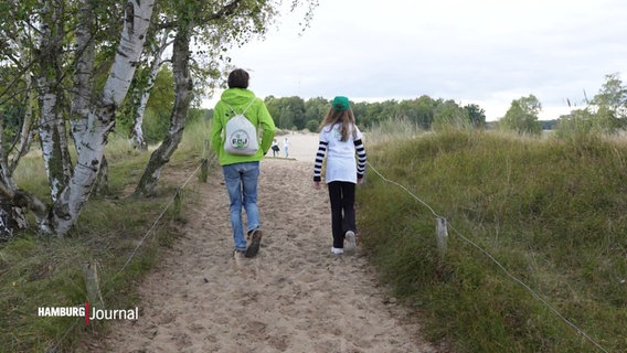 Ein Mann mit grüner Jacke und ein Kind gehen durch die Dünen. © Screenshot 