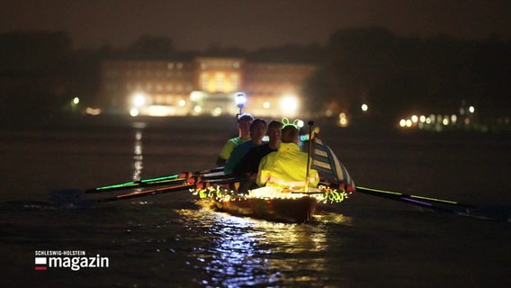 Ein mit Lichterketten geschmücktes Boot bei der Lichterfahrt von Schüler-Rudervereinen auf der Kieler Förde. © Screenshot 