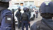 Mehrere Einsatzkräfte der Polizei stehen in schwerer Schutzausrüstung mit Helmen auf einem öffentlichen Platz. © Screenshot 