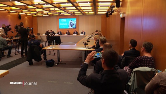 Viele Menschen sitzen bei einer Pressekonferenz in einem Raum. © Screenshot 