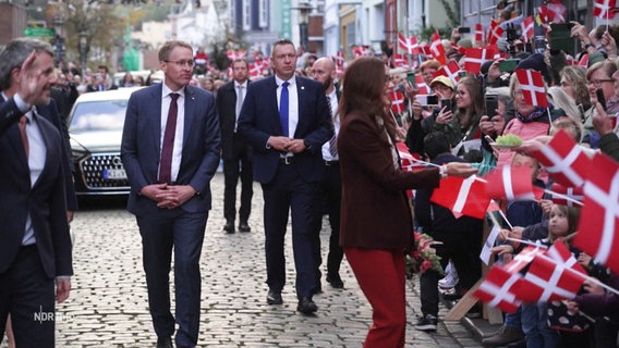 In einem Tross gehen das dänische Königspaar und Schleswig-Holsteins Ministerpräsident Daniel Günther (CDU) an vielen mit dänische Flaggen wedelnden Menschen vorbei. © Screenshot 