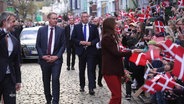 In einem Tross gehen das dänische Königspaar und Schleswig-Holsteins Ministerpräsident Daniel Günther (CDU) an vielen mit dänische Flaggen wedelnden Menschen vorbei. © Screenshot 