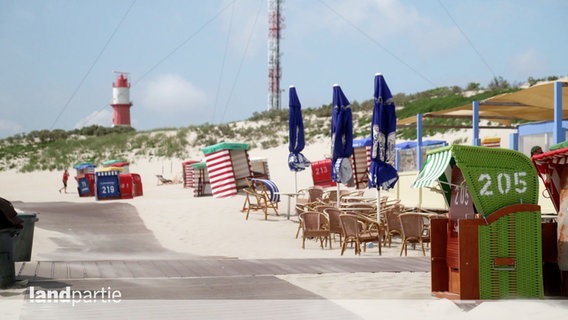 Eine Strandpromenade mit weißem Sandstrand, Strandkörben und Leuchtturm im Hintergrund. © Screenshot 