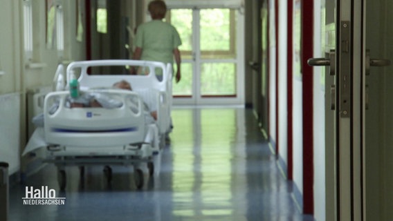 Ein Patientenbett steht auf einem Krankenhausflur, dahinter steht eine Krankenschwester. © Screenshot 