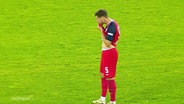 Ein Spieler von Hansa Rostock steht sichtlich niedergeschlagen auf einem Fußballplatz und wischt sich mit dem Trikot über das Gesicht. © Screenshot 