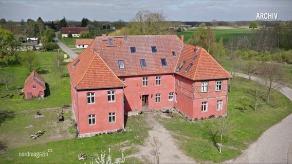 Ein markantes, rotes Herrenhaus auf einer Wiese. © Screenshot 