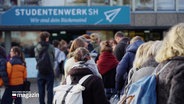 Studierende von hinten, im Hintergrund das blau-weiße Banner des "Studentenwerk SH". © Screenshot 