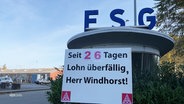 Das Logo der Werft FSG, darunter ein Plakat: "Seit 26 Tagen überfällig, Herr Windhorst!" © Screenshot 