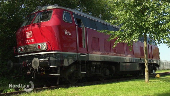 Ein älteres Modell einer Zuglokomotive steht auf einem Gleis vor einem kleinen Waldstück. © Screenshot 