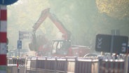 Im Nebelstaub einer Baustelle arbeitet ein Bagger an einer Straßenausbesserung. © Screenshot 