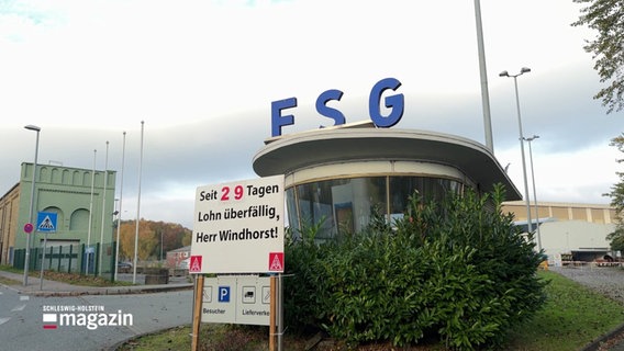 Pförterhaus an einer FSG-Werft. Davor ein Schild von der Gewerkschaft IG Metall. Darauf steht: "Seit 29 Tagen Lohnüberfällig, Herr Windhorst!" © Screenshot 