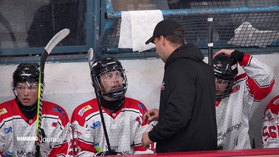 Eishockey-Spieler der Crocodiles Hamburg besprechen sich während eines Spiels auf der Bank. © Screenshot 