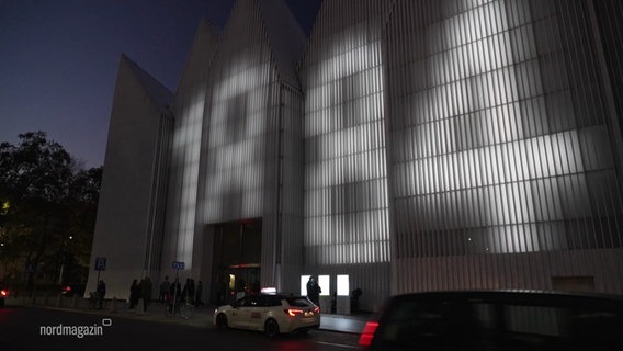 Außenansicht der modernen Stettiner Philharmonie. Auf der weißen, geriffelten Oberfläche leuchten Lichter die Zahl 1884 auf die Fassade. © Screenshot 