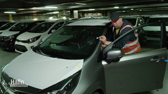 Ein Mann in Warnweste schiebt ein defektes Auto auf einem Parkdeck. © Screenshot 