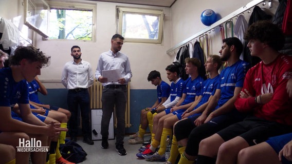 In einer Umkleidekabine sitzen mehrere Jungen einer Fußballmannschaft zur Teambesprechung. © Screenshot 