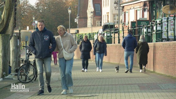 Mehrere Passantinnen und Passanten gehen eine Hafenpromenade entlang. © Screenshot 