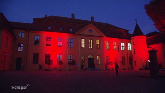 Ein historisches Stadtgebäude ist in rotem Scheinwerferlicht angeleuchtet. © Screenshot 