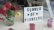 In einem Schaufenster steht ein Schild: "Summer of Pioneers". © Screenshot 