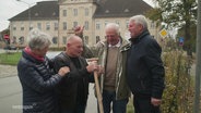 Drei Männer und eine Frau stehen zusammen, einer von ihnen hält einen Spaten in der Hand. © Screenshot 