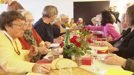 Menschen sitzen zusammen an einem langen Tisch und essen. © Screenshot 