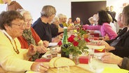 Menschen sitzen zusammen an einem langen Tisch und essen. © Screenshot 