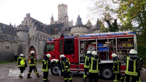 Mehrere Einsatzkräfte der Feuerwehr bereiten sich auf einen Übungseinsatz mit ihrem Drehleiterwagen vor der Marienburg vor. © Screenshot 