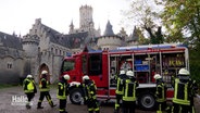 Mehrere Einsatzkräfte der Feuerwehr bereiten sich auf einen Übungseinsatz mit ihrem Drehleiterwagen vor der Marienburg vor. © Screenshot 