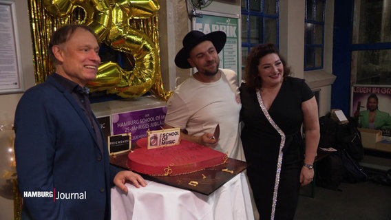 Saänger und Schirmherr der Hamburg School of Music posiert für ein Foto vor einem Kuchen in Herzform. © Screenshot 