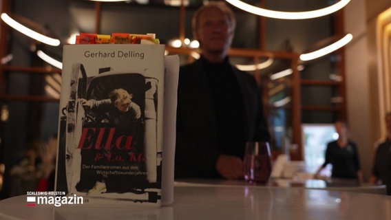 Das Buch "Ella & Co. KG" im Vordergrund. Sein Autor Gerhard Delling verschwommen im Hintergrund. © Screenshot 