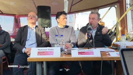 Drei Politiker sitzen bei einer Pressekonferenz auf einer Barkasse vor einem Tisch. © Screenshot 